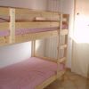 Letto a castello in legno con coperte rosa in una stanza luminosa con pavimento piastrellato.