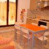 Cucina con tavolo arancione, sedie bianche, divano arancione e mobili chiari.