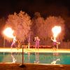 Spettacolo notturno di giocolieri col fuoco vicino a una piscina.