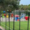 Campo sportivo con rete da calcio e parco giochi colorato recintato.