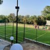 Un campo da calcio all'aperto con recinzione e un gruppo di persone lungo la linea laterale.