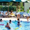 Persone nuotano in piscina mentre due adulti ballano a bordo vasca.