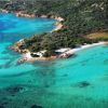 Spiaggia con acqua cristallina e vegetazione verde, vista aerea di una costa rocciosa.