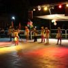 Bambini in costume seguono una donna in rosso su un palco illuminato.