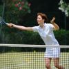Una donna in divisa bianca colpisce una palla da tennis su un campo.