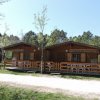 Due casette di legno affiancate con verande, circondate da alberi e erba.