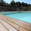 Piscina con acqua azzurra e bordo in legno, circondata da alberi.
