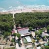 Vista aerea di una località costiera con case e piscina, circondata da foresta e spiaggia.
