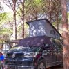 Camper nero con tetto rialzato in un'area alberata.