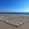 Ampia spiaggia con file di ombrelloni bianchi.