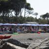 Spiaggia con sdraio e ombrelloni blu, con alberi sullo sfondo.