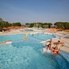 Un gruppo di quattro persone si diverte in una piscina, circondata da ombrelloni e sdraio colorati.