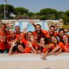 Un gruppo di persone sorridenti in magliette arancioni posa felice in una piscina.