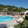 Una piscina contornata da lettini e ombrelloni, con un edificio basso e colline verdi sullo sfondo.