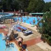 Piscina affollata con scivoli e lettini. Alberi sullo sfondo.