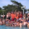 Grande gruppo di persone festanti in piscina, alcune in divise arancioni.