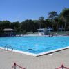 Piscina all'aperto con persone che nuotano, circondata da alberi.