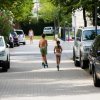 Bambini corrono su un vialetto con auto parcheggiate.