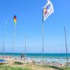 Spiaggia con bandiere e ombrelloni colorati.