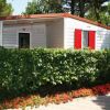 Un bungalow bianco con persiane rosse, circondato da una siepe e bordure di fiori.